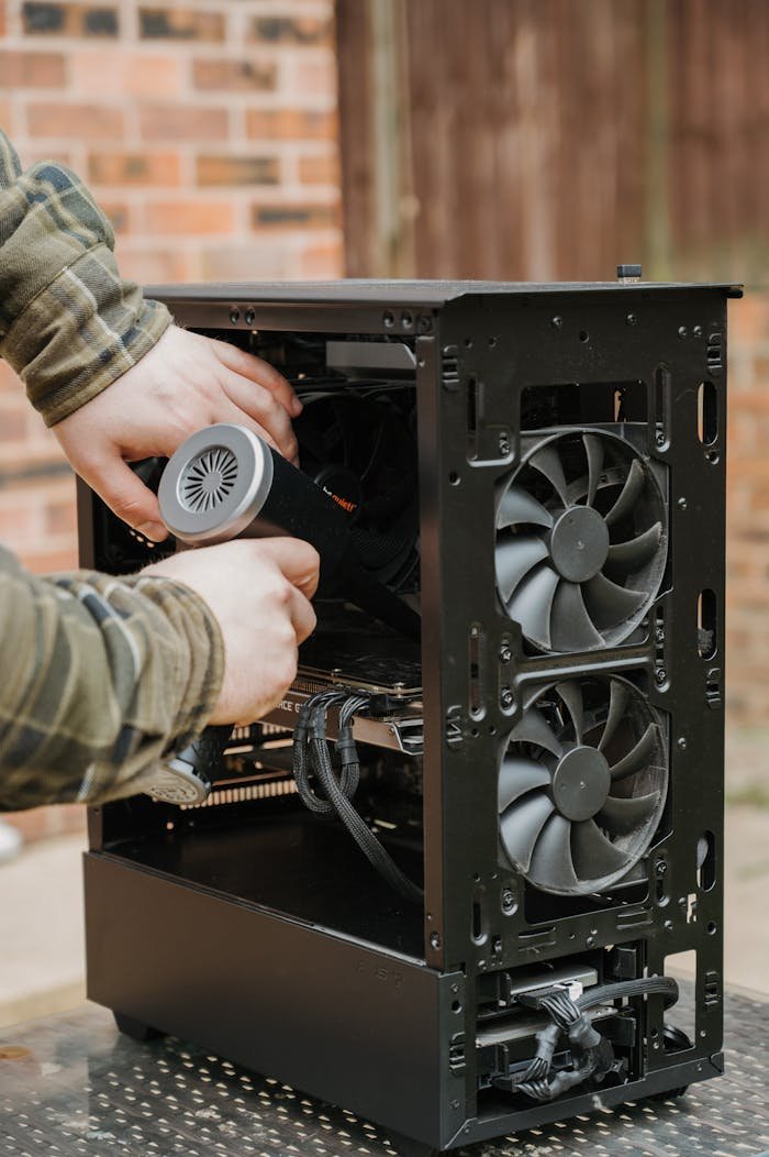 Hands cleaning a desktop PC case with an electric duster outdoors.